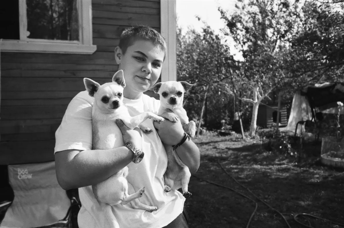 A person holding two small chihuahuas in their arms outside a home